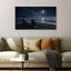 Beach scene with chairs and candles on a wall above a sofa with decorative pillows.