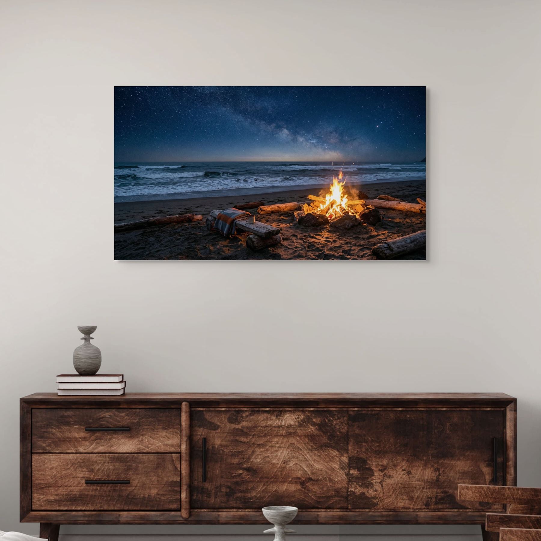 Framed artwork of a beach scene with a campfire above a wooden dresser.