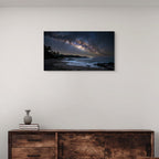 Canvas artwork of a night sky over a beach on a white wall above a wooden cabinet.