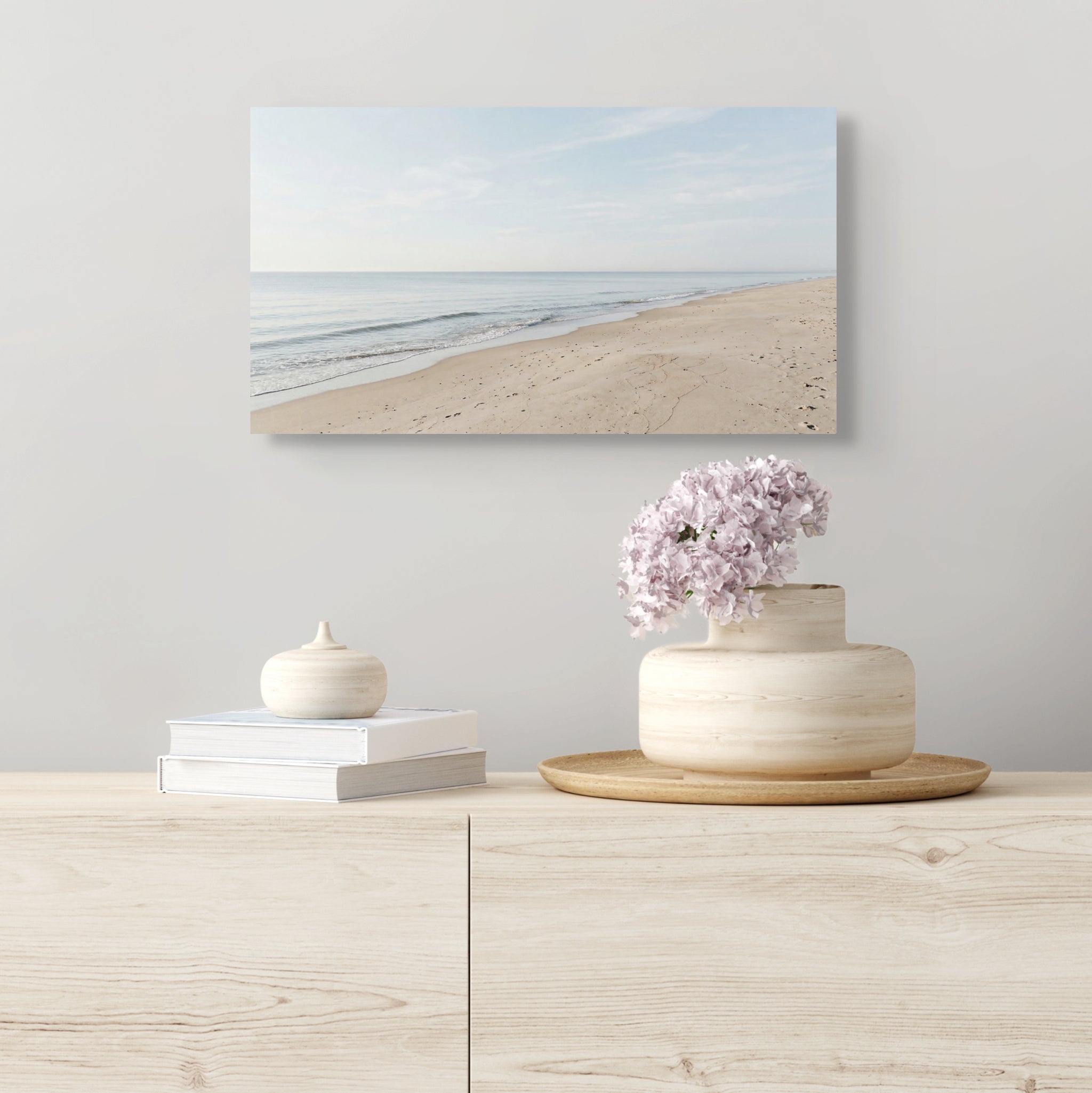 Decorative setup with a vase of flowers, books, and a small sculpture on a wooden surface, with a beach-themed wall art in the background.