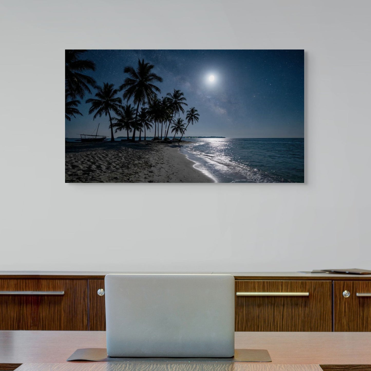 Tropical beach scene canvas wall art with palm trees and moonlit sky on a wall above a desk.
