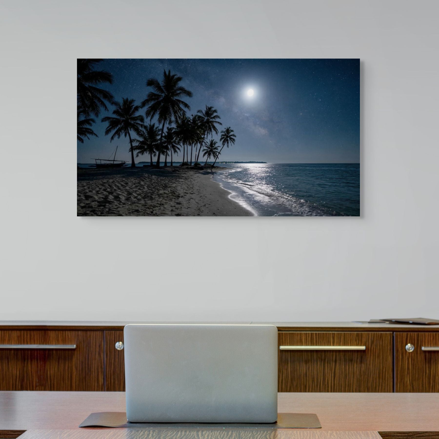 Tropical beach scene canvas wall art with palm trees and moonlit sky on a wall above a desk.