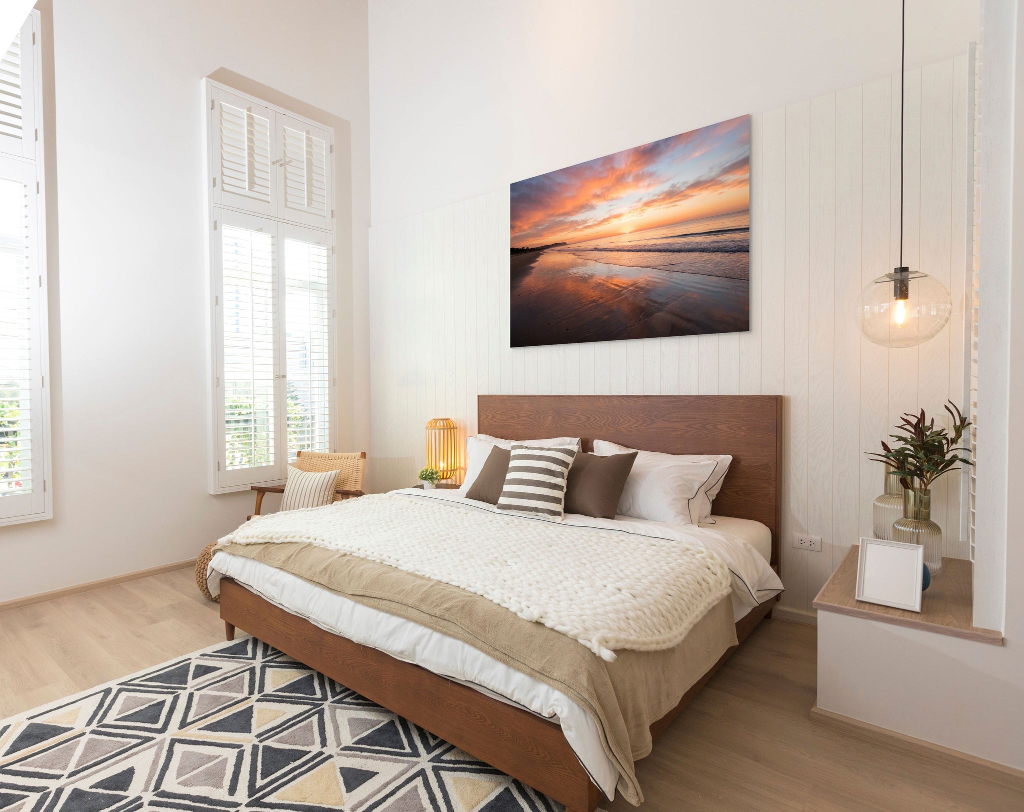 Modern bedroom with wooden bed, decorative pillows, and a sunset painting on the wall.