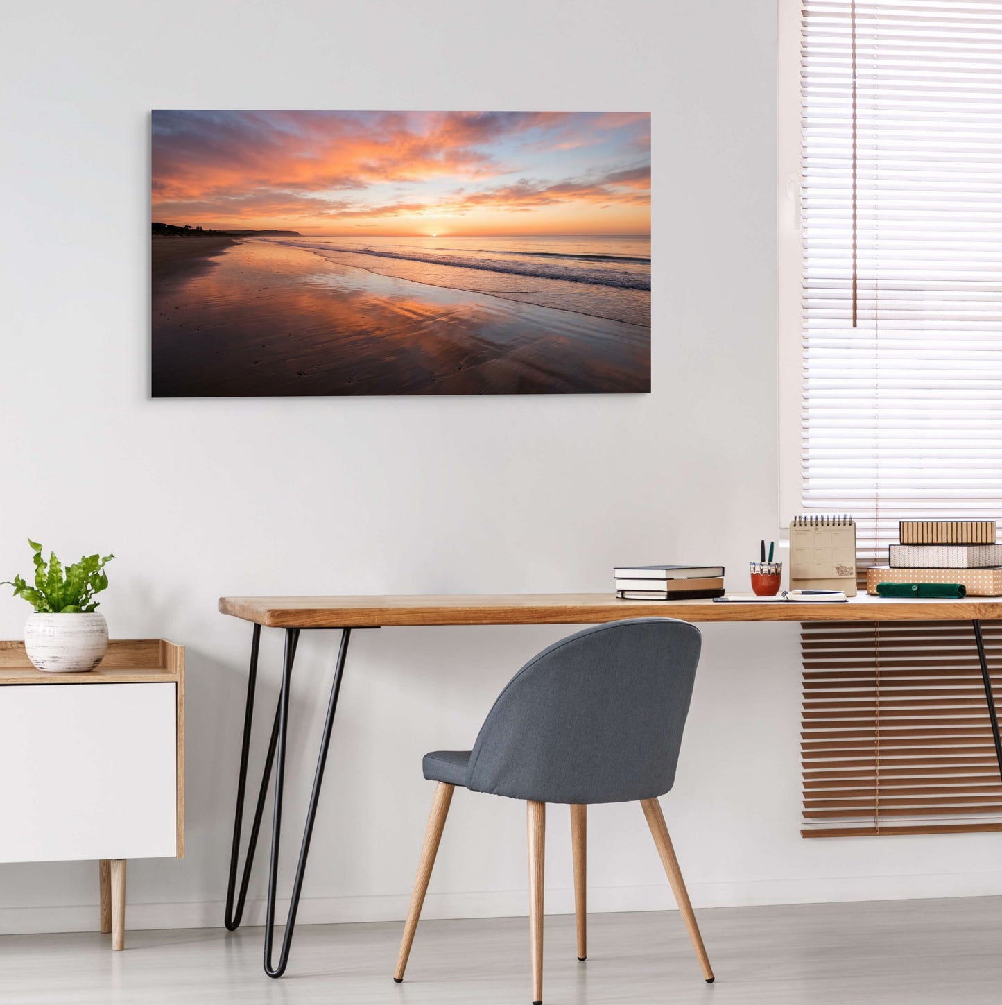 Modern home office with a desk, chair, and large wall art of a sunset over water.