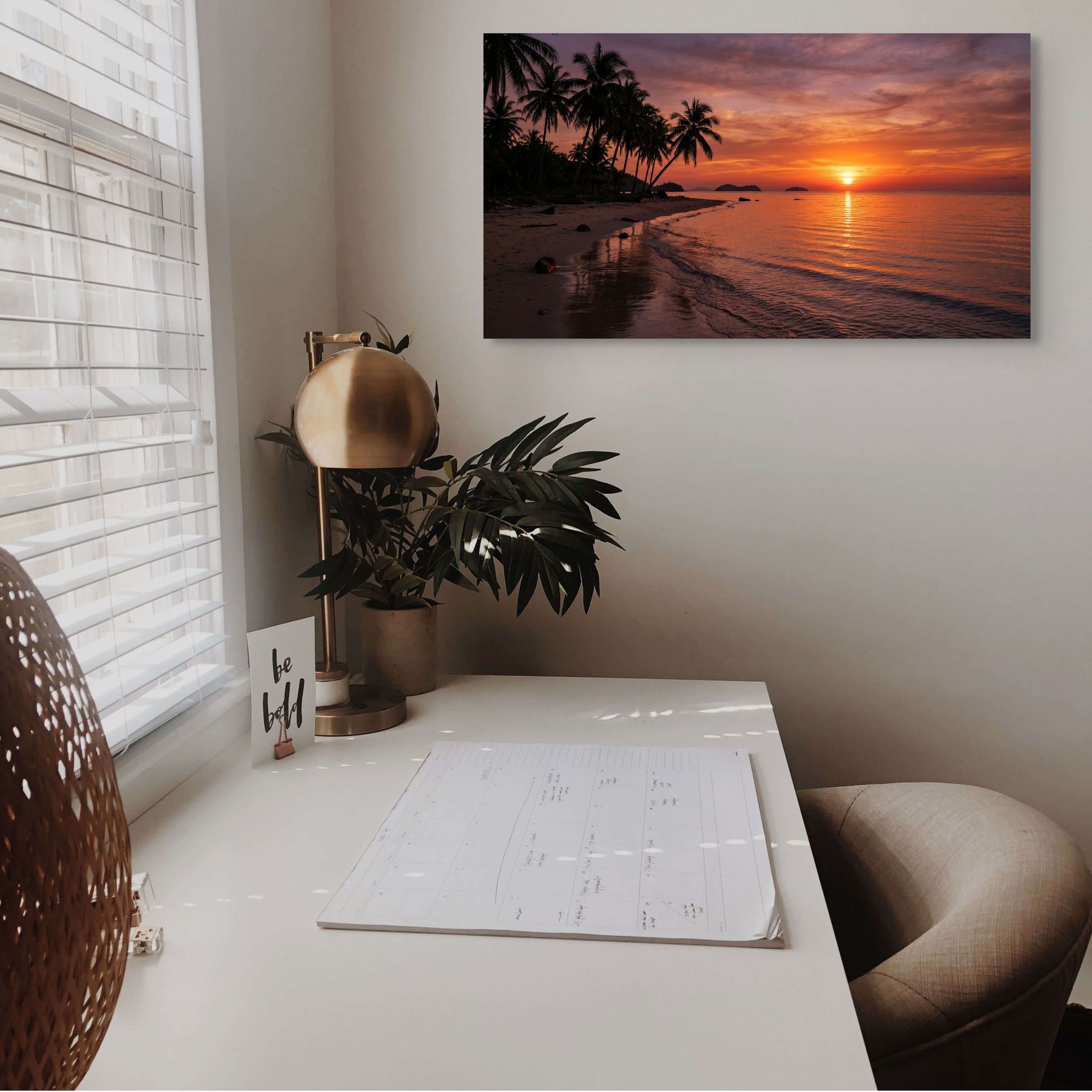 Home office with a desk, plant, and wall art of a sunset over water.